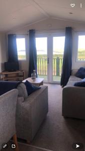 a living room with a couch and a table and windows at Gwel y Môr - Lleyn Peninsula Static in Llangwnadl