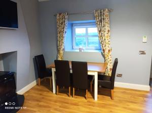 mesa de comedor con sillas negras y ventana en Cosy 1 bedroom cottage, Ideal quiet getaway. en Creeslough