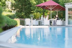 eine Gruppe von Menschen, die unter einem Schirm am Pool sitzen in der Unterkunft Ludinmühle in Freiamt