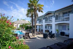 a resort with a pool and palm trees and chairs at Hôtel Le Peu Breton in Sainte-Marie-de-Ré