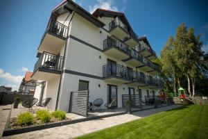 a white building with black balconies and a yard at Jakubowa Polana - pokoje in Łeba