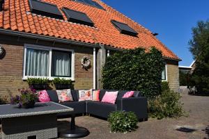 OosterendにあるHotel Dichtbijzeeのピンクの枕が備わる家の外に座るソファ