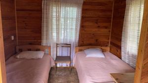 two beds in a room with wooden walls and windows at Veccepļi kempings in Spāre