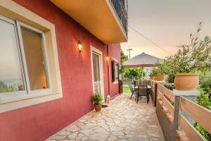 Cette maison rouge dispose d'une terrasse avec une table et des chaises. dans l'établissement Alesti House with garden and private beach access, à Benitses