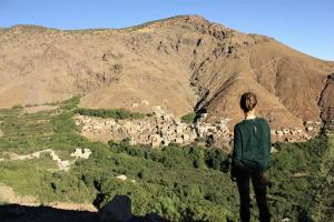 une femme debout au sommet d'une montagne et regardant un village dans l'établissement Gite Tizi Mizik, à Imlil