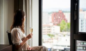 uma mulher segurando um copo de vinho olhando pela janela em Daiwa Roynet Hotel Morioka Ekimae em Morioka