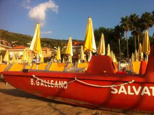 een rode boot met gele parasols op het strand bij Hotel Galleano in Marina dʼAndora