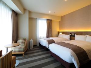 a hotel room with two beds and a chair at Far East Village Hotel Yokohama in Yokohama