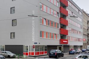 un edificio con ventanas rojas y coches aparcados en un aparcamiento en MEININGER Hotel Wien Downtown Sissi, en Viena