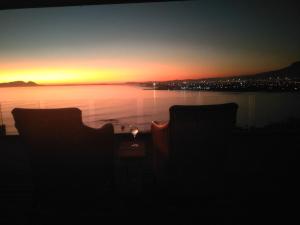 una puesta de sol sobre el agua con dos sillas y una mesa en Palm Tree Self-Catering Apartment, en Gordonʼs Bay