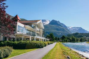 a building next to a river with mountains in the background at Hotel Loenfjord Loen in Loen