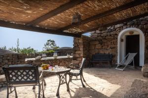 a patio with a table and chairs and a stone wall at Tenuta Dammuso Soledad in Scauri