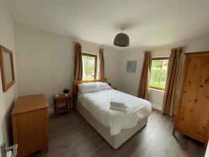 a bedroom with a white bed and two windows at No 2 Ardnagashel Woods in Ballylickey