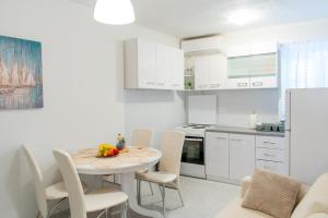cocina con armarios blancos, mesa y sillas en Apartman Karmen, en Kaštela