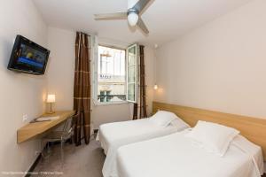 a hotel room with two beds and a desk and a television at Hotel Gambetta in Bordeaux