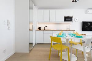 a white kitchen with a table and yellow chairs at JANTAR APARTAMENTY Posesja Kapitańska in Grzybowo