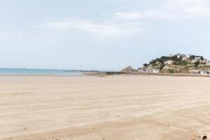 a sandy beach with houses on a hill in the distance at Les Bleuets - Duplex avec vue mer in Pléneuf-Val-André