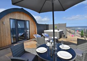 eine Terrasse mit einem Tisch, Stühlen und einem Sonnenschirm in der Unterkunft 2 Sinclair bay lodges in Keiss