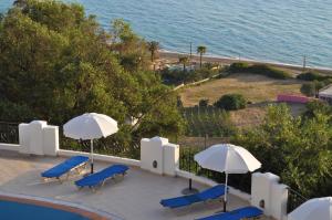 a patio with chairs and umbrellas and the ocean at Apartments Maria with Amazing Pool - Agios Gordios Beach in Agios Gordios