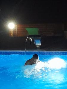 mężczyzna pływa w basenie w nocy w obiekcie Apartmani Žuti Leptir w mieście Vrdnik