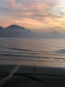 una persona caminando por la playa al atardecer en Astúrias Top Apartamento, en Guarujá