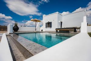 a white house with a swimming pool and an umbrella at Vineyard Exclusive Suites in Akrotiri