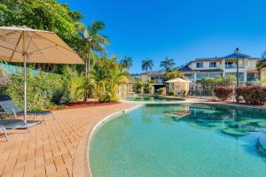 a patio area with a pool, chairs, and a patio umbrella at Aqualuna Beach Resort in Coffs Harbour