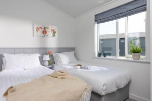zwei Betten in einem weißen Zimmer mit Fenster in der Unterkunft Buttercup Lodge, 33 Roadford Lake Lodges in Lifton