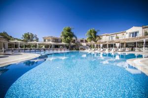 una grande piscina con sedie bianche e alberi di Villas Resort Wellness & SPA a Castiadas