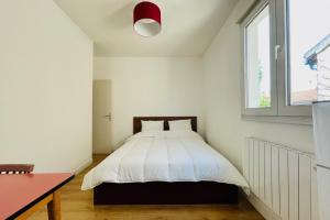 Schlafzimmer mit einem Bett mit weißer Bettwäsche und einem Fenster in der Unterkunft Appart'Hôtel l'Express - 25min de Paris in Romainville