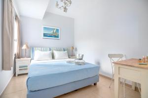 a white bedroom with a blue bed and a desk at Arolithos in Spetses