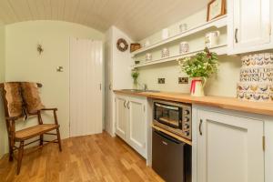 una cocina con armarios blancos y una silla. en Woodland Retreat Shepherd's Hut en Brundish