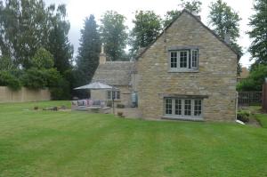 a stone house with a lawn in front of it at Gardeners Cottage in Shipton under Wychwood