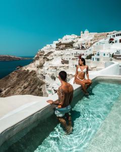 a man and a woman standing on a beach next to a pool at Echoes Luxury Suites in Oia
