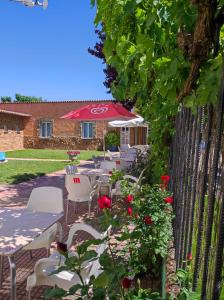 un patio con sillas blancas, una sombrilla y rosas en Albergue Santa Ana, en San Martín del Camino