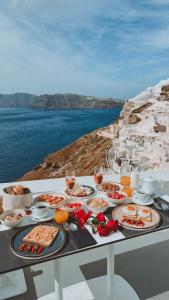 a table with food and glasses of wine on a cliff at Echoes Luxury Suites in Oia