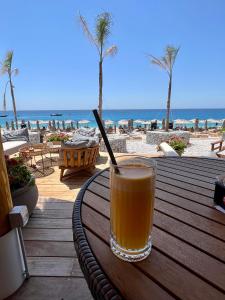 a glass of juice sitting on a wooden table at the beach at Royal Paradise Green Coast Resort Palase in Vlorë