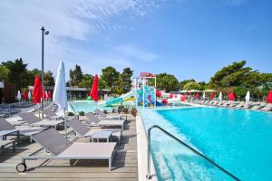 a pool filled with lots of chairs and umbrellas at Hotel Sipar Plava Laguna in Umag