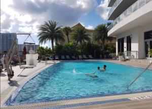 two people swimming in a large swimming pool at Miami Beach Glam, Ocean Views & Elegance -28B in Hallandale Beach