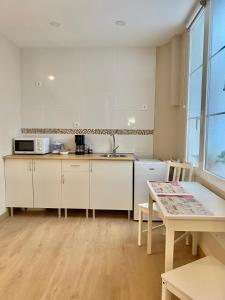 a kitchen with white cabinets and a sink and a table at Alojamientos Muelle de Gijón in Gijón