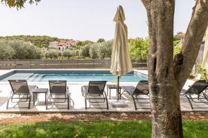 een groep stoelen en een parasol naast een zwembad bij Apartments Tina Stinjan in Pula