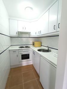 - une cuisine blanche avec évier et cuisinière dans l'établissement Acogedor apartamento a 50 metros de la playa, à Isla Canela
