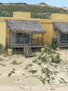 a yellow building with a porch and a straw roof at Bangalô Encantador Praia da Baleia in Itapipoca