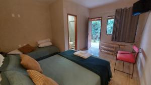 1 dormitorio con 2 camas y silla roja en Recanto dos Ipês Pousada, en Divisa