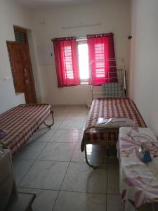 a room with two beds and a window with red curtains at Suloram illam in Chidambaram