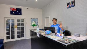a man sitting at a desk with his hand up at Silver Oaks Motel in Gilgandra