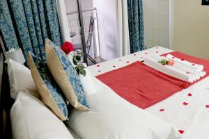 uma cama branca com um cobertor vermelho e flores em Tribute Guest House Matala em Maseru