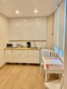 a kitchen with white cabinets and a sink and a table at Alojamientos Muelle de Gijón in Gijón