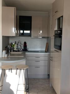 una cocina con armarios blancos, fregadero y 2 taburetes en Petit appartement cosy en Villers-sur-Mer