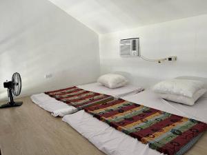 two beds in a white room with a fan at Manzil Jina Laiya House Rental in San Juan